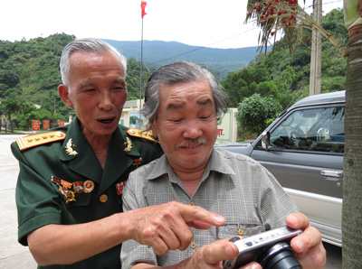 Họa sĩ Đức Dụ (bên phải) cùng anh hùng gùi thồ Nguyễn Viết Sinh vui cười phát hiện địa điểm họ đi qua từ trong một khuôn hình chụp.